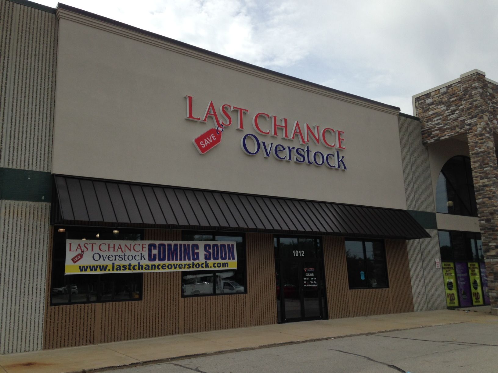 Storefront sign for Last Chance Overstock on a strip mall building with a “Coming Soon” banner