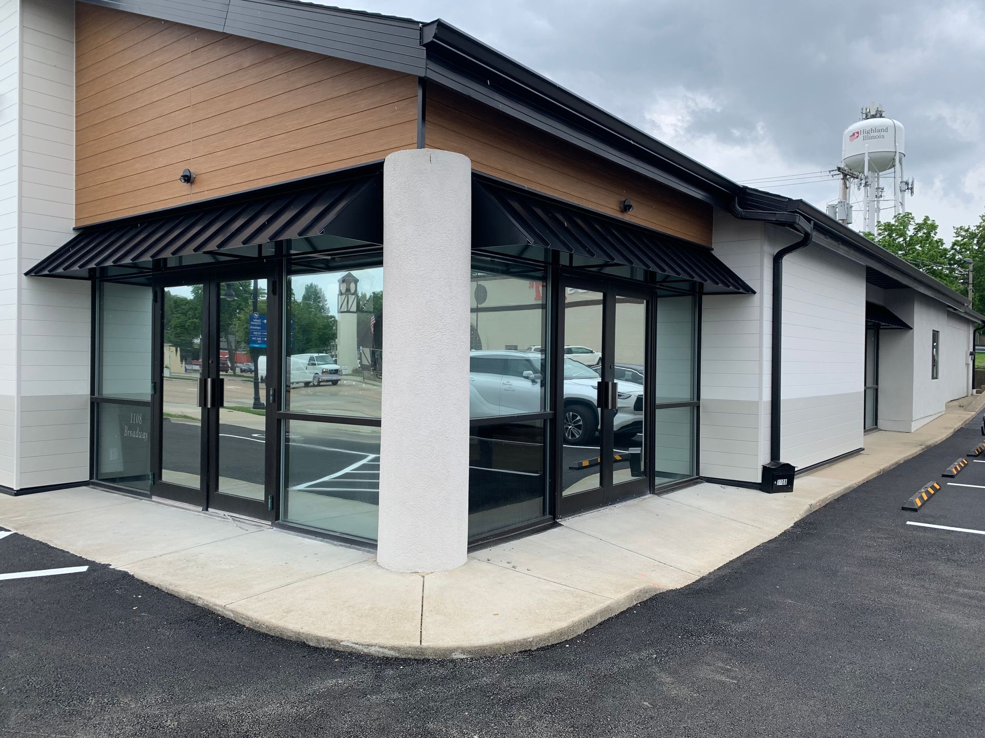 Corner view of a modern empty storefront with glass windows, black awning, and white walls.