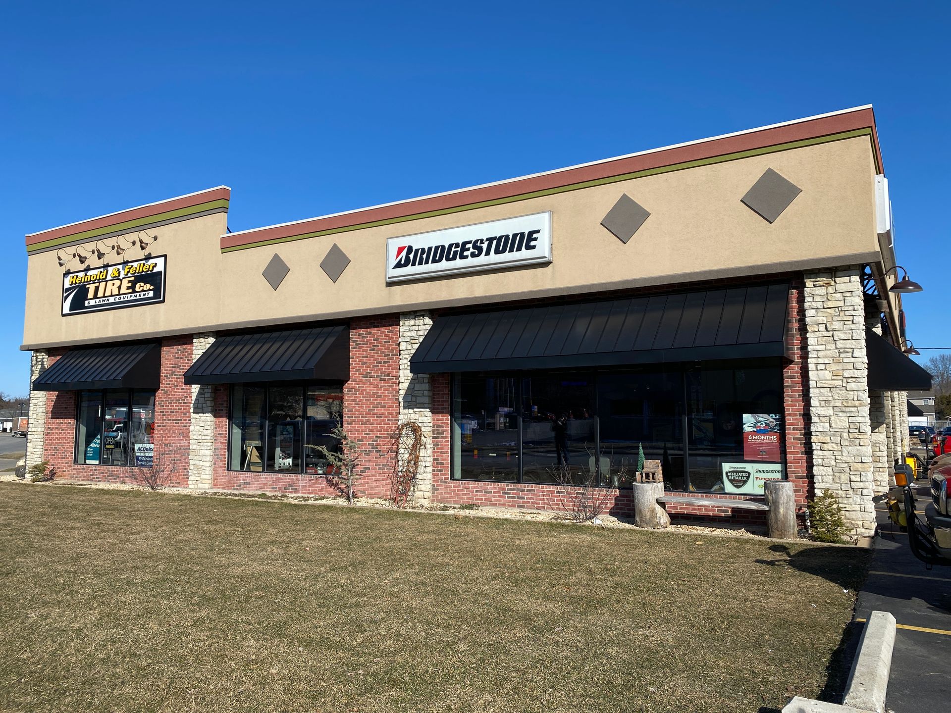 Strip mall storefront with a Bridgestone sign, awnings, stone columns, and windows under a clear sky