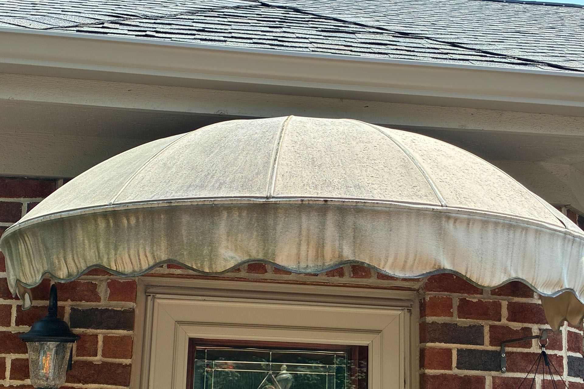 Beige scalloped awning over a brick house window and wall