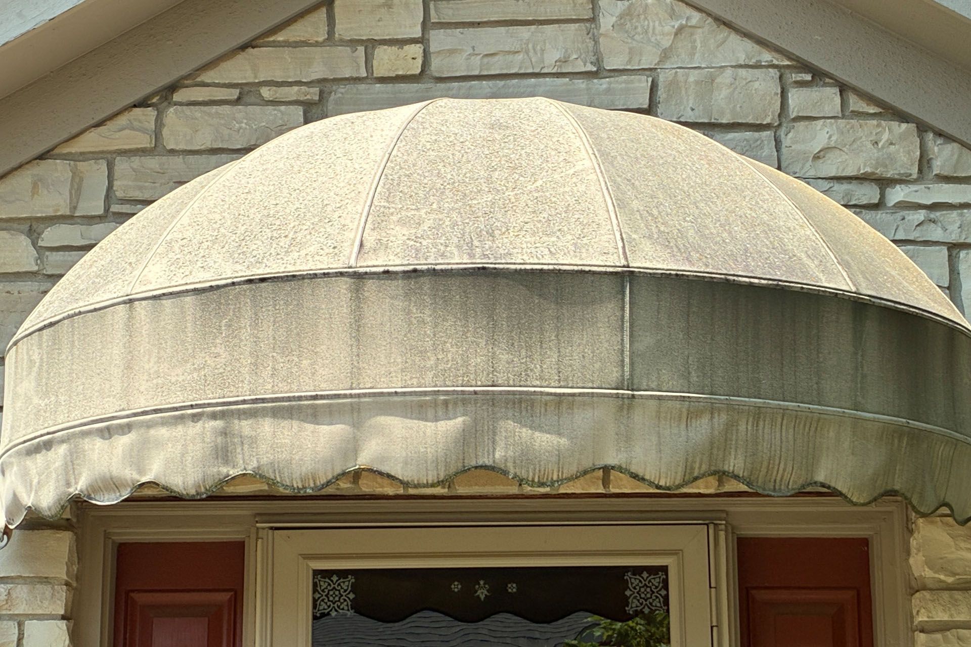 Beige awning over a doorway beneath a stone exterior wall