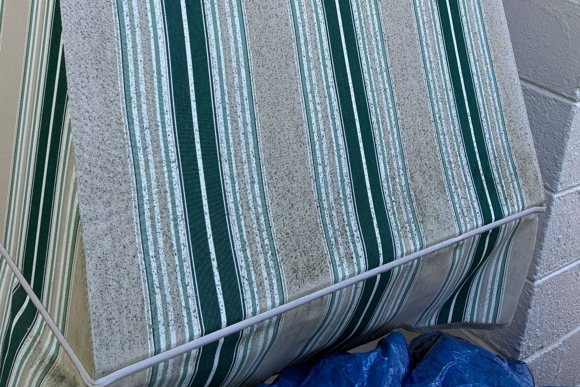 Striped outdoor cushion or mat with teal, beige, and gray stripes leaning against a tiled wall