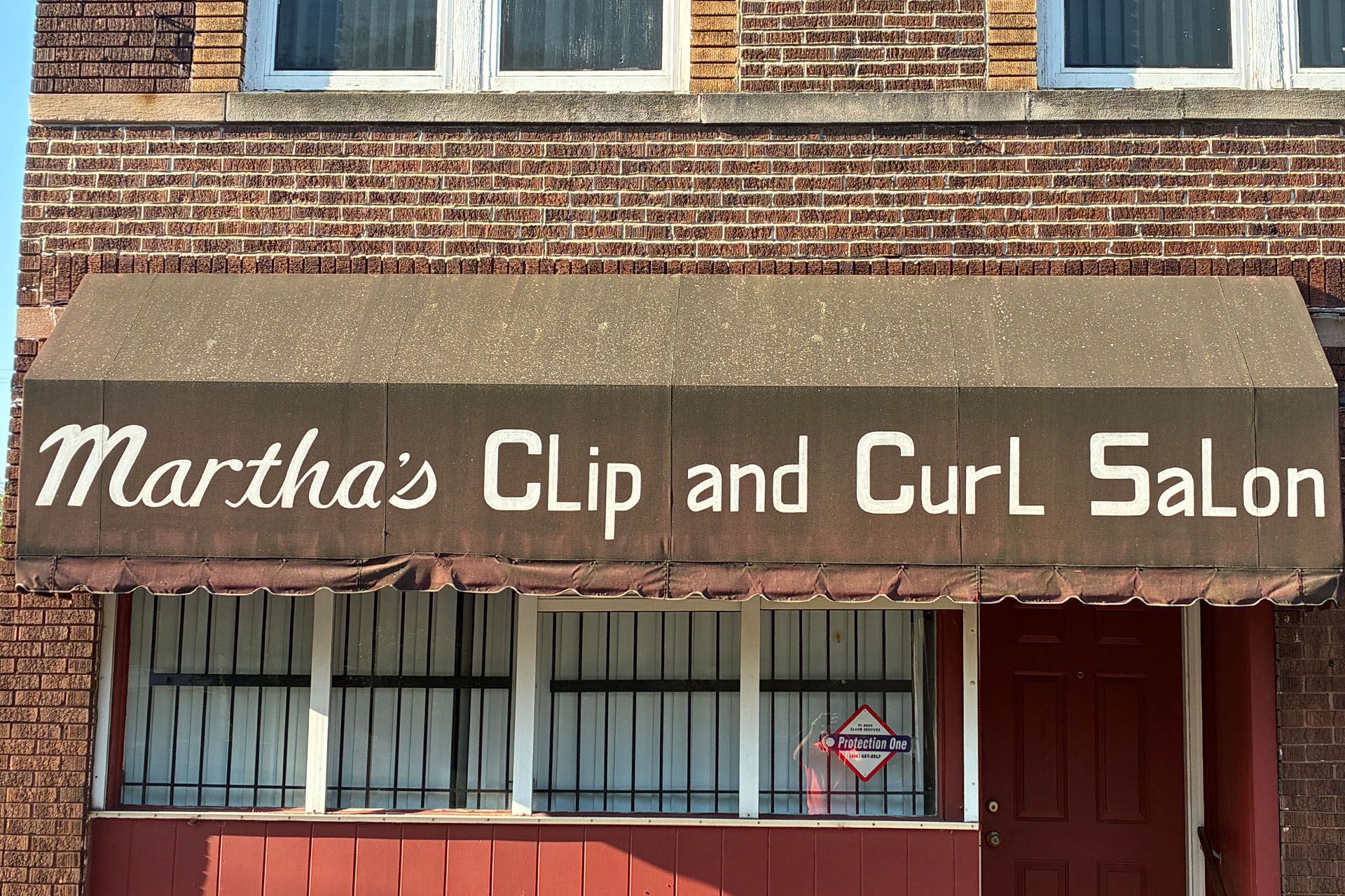 Storefront sign reading “Martha’s Clip and Curl Salon” on a brick building.