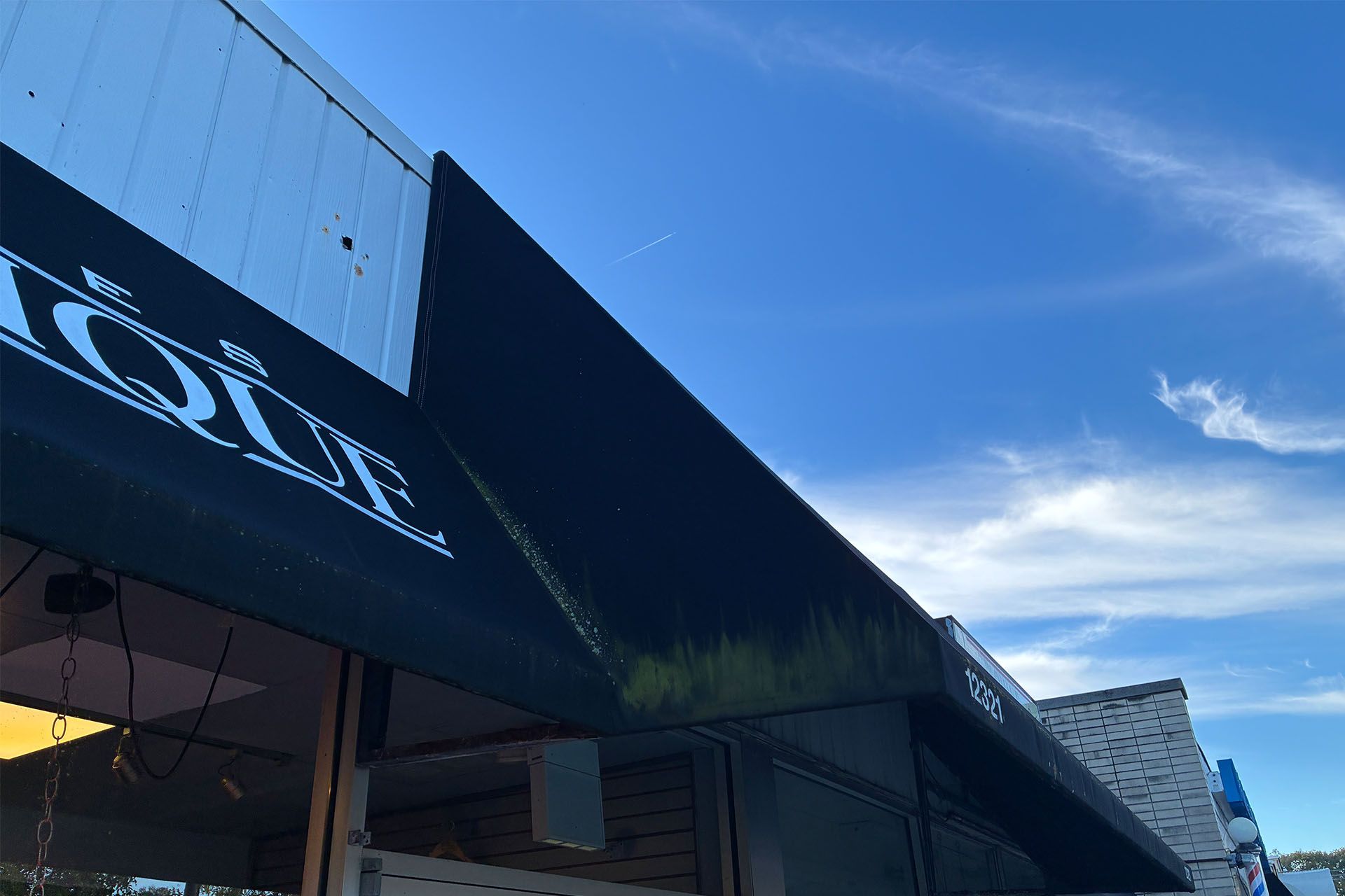 Black storefront awning with white logo against a bright blue sky with wispy clouds