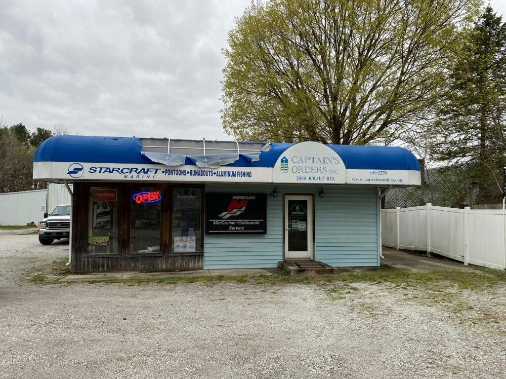 Small roadside auto service shop with blue awning, neon open sign, and gravel parking lot.