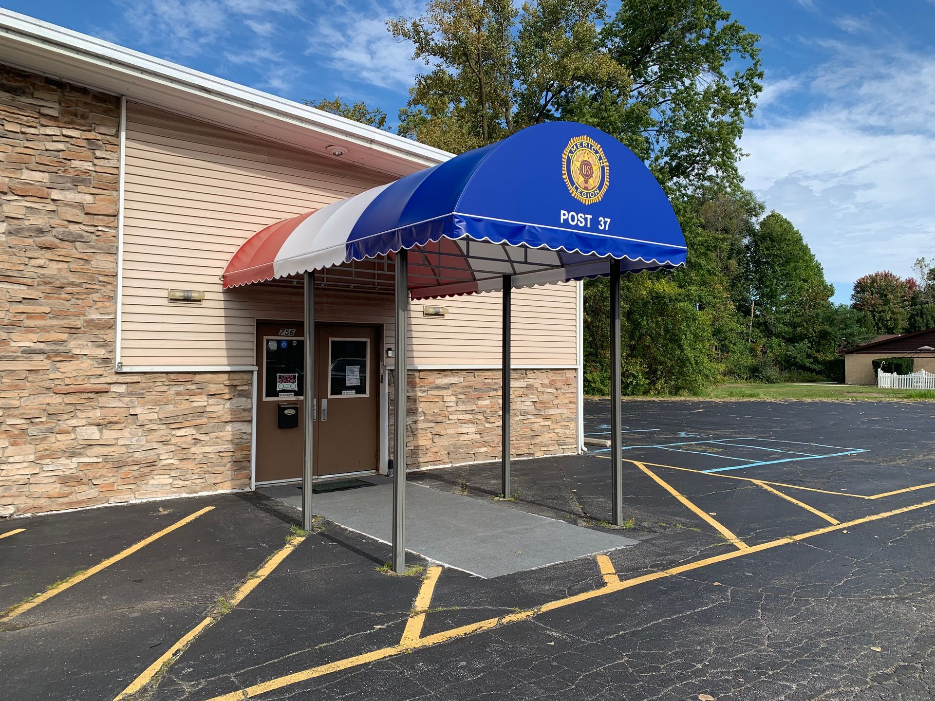 Brick building entrance with blue canopy over an accessible ramp and parking lot markings