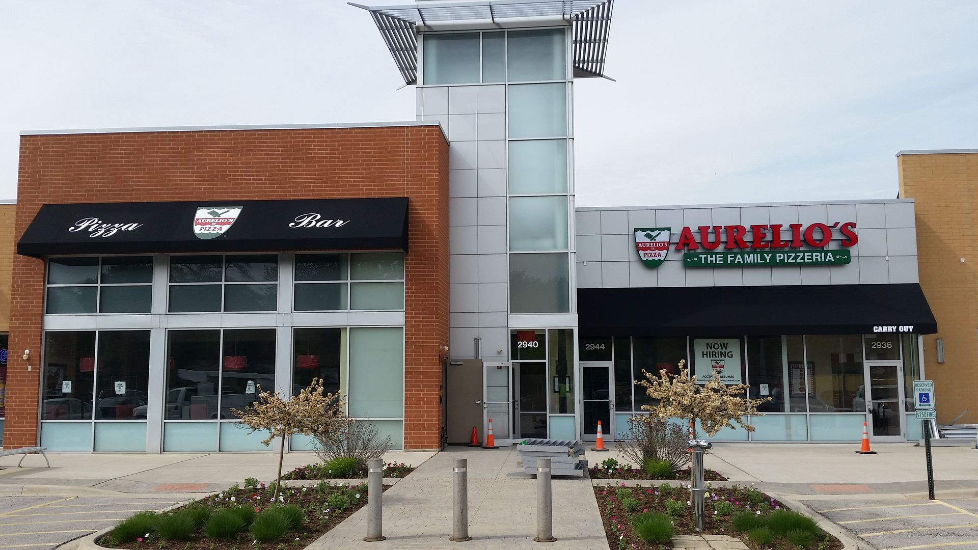 Strip mall storefronts with glass doors, black awning, and a central elevator tower.