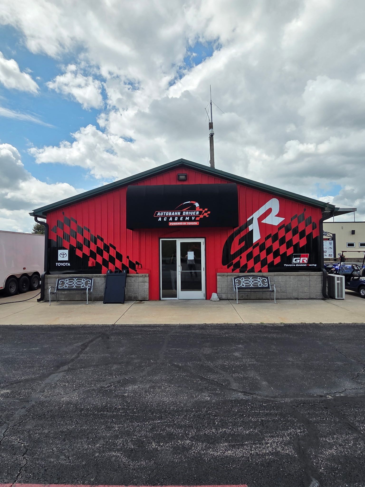 Red storefront with checkered racing graphics and a white logo under a cloudy sky.