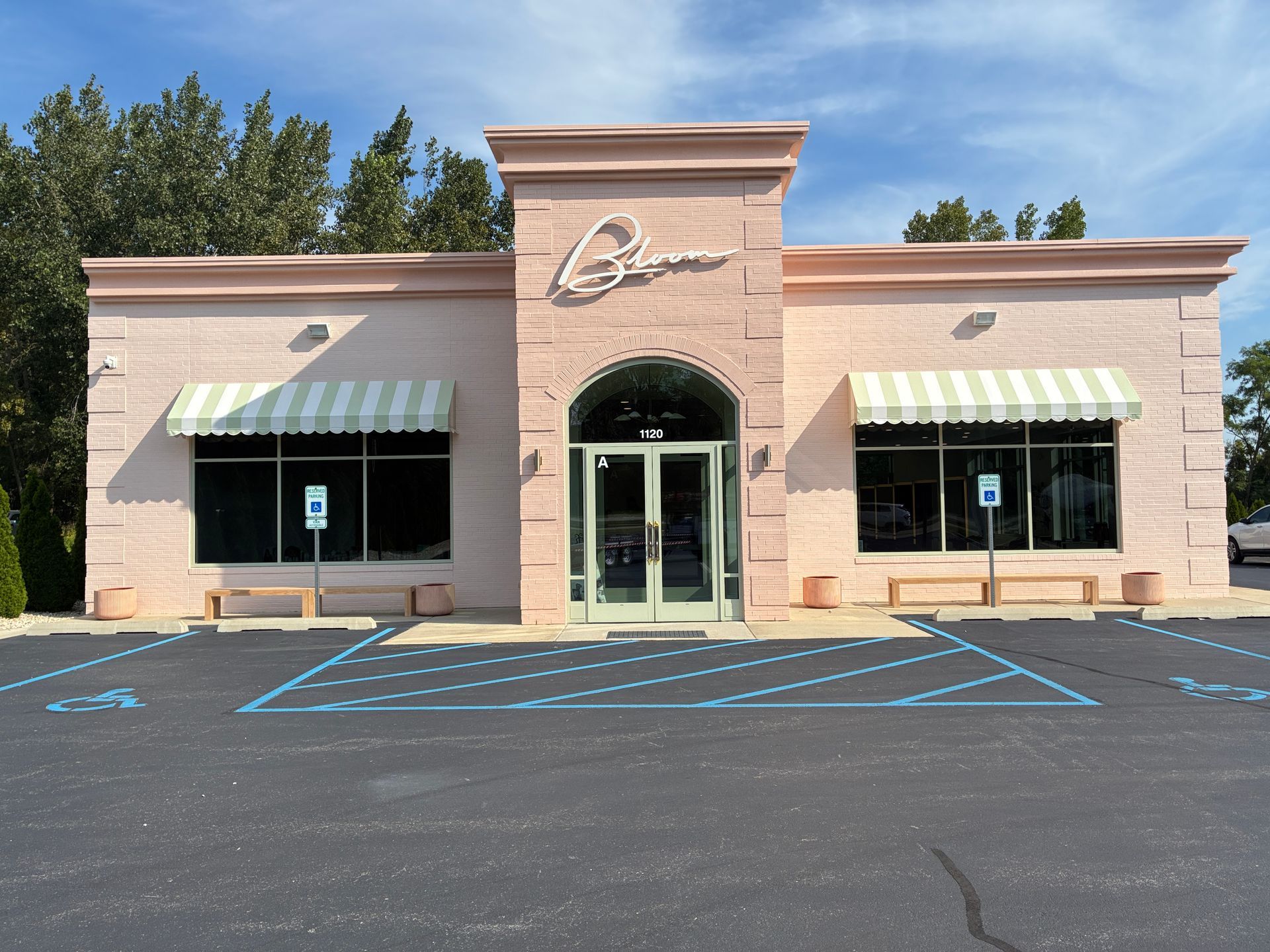 Front view of a beige storefront with striped awnings and a central arched entrance, seen from an empty parking lot