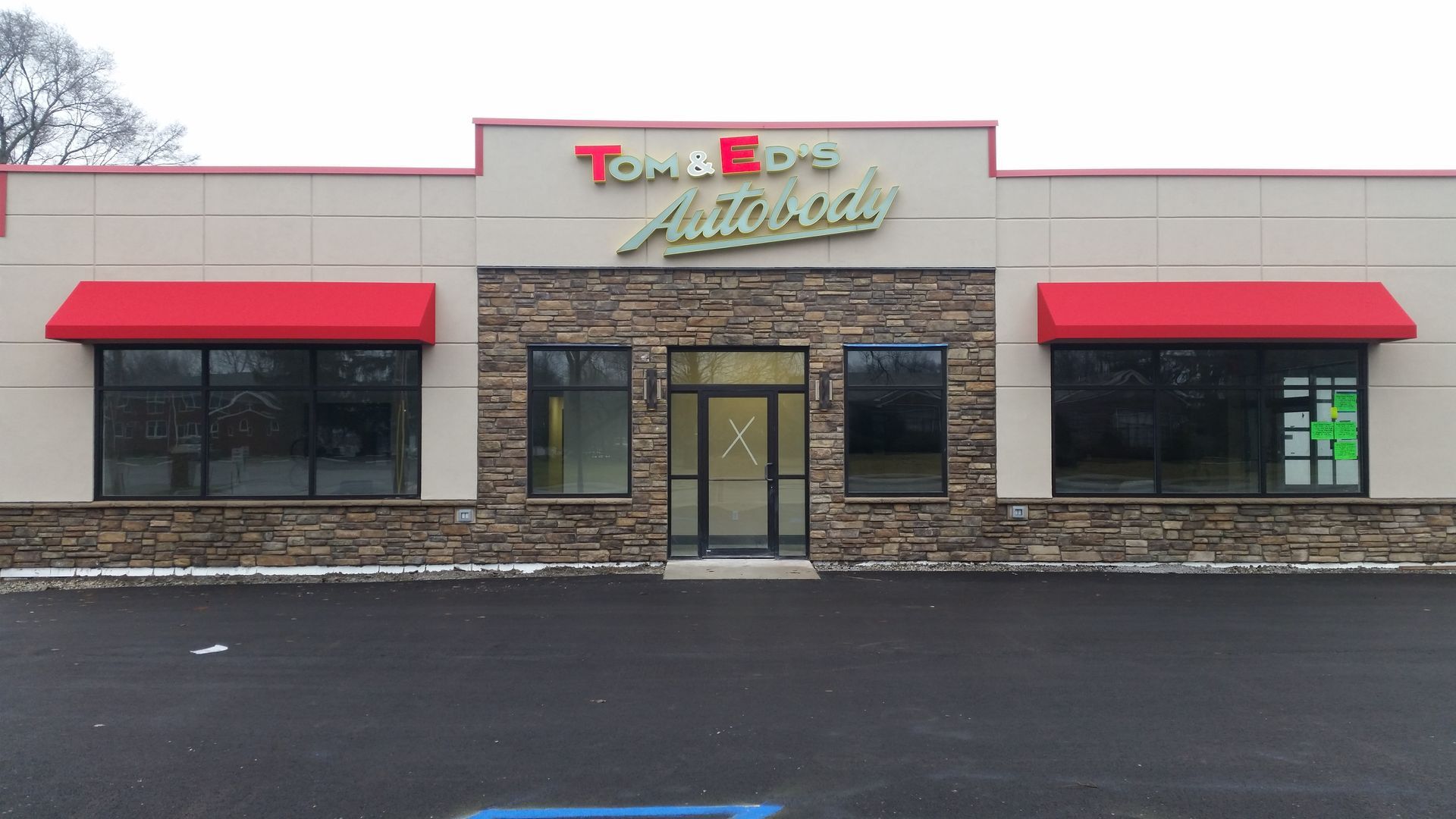 Front view of a strip mall storefront with red awnings and stone facade on a wet parking lot.