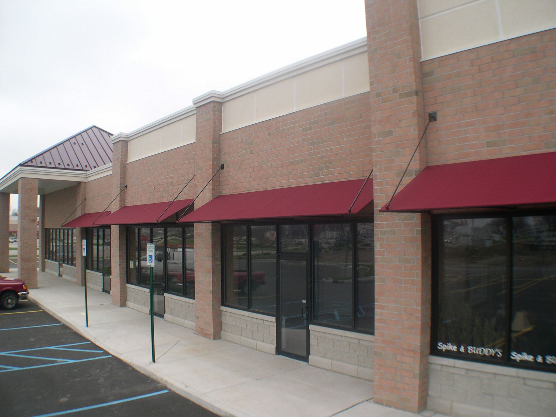 Strip-mall storefronts with red awnings and dark windows along a covered sidewalk