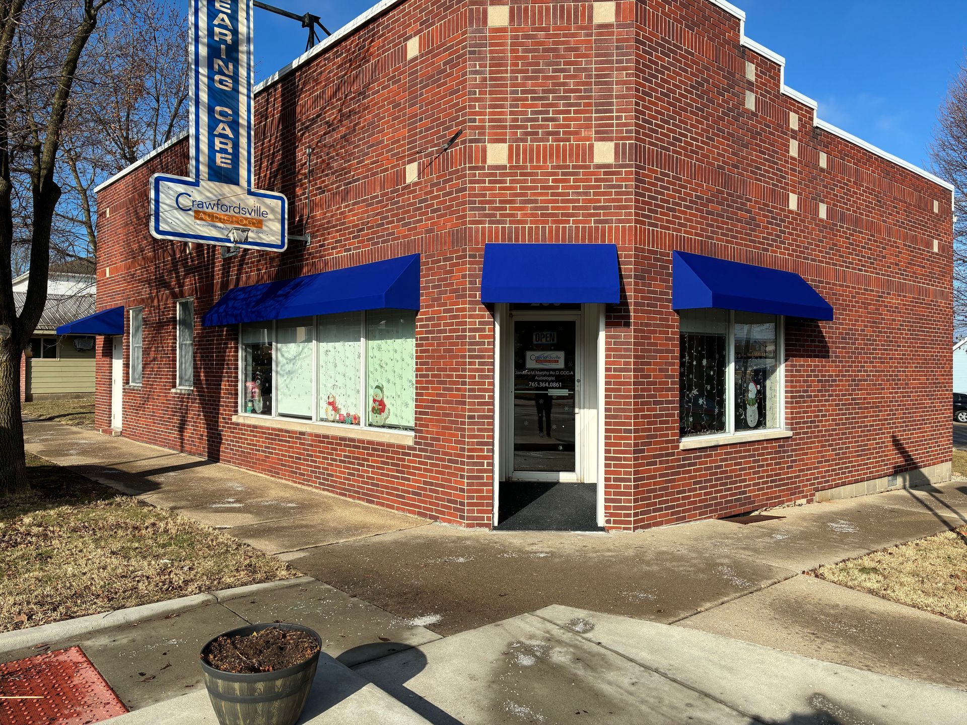 Small red brick storefront with blue awnings on a corner sidewalk under a clear blue sky