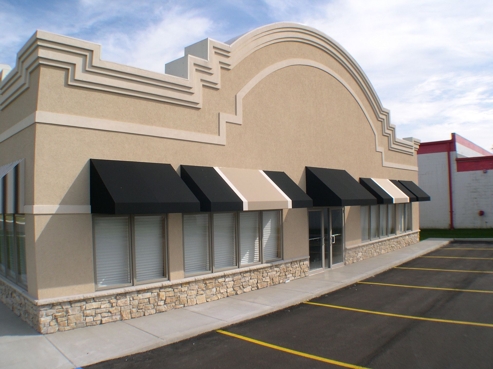Empty storefront with black awnings and beige facade in a parking lot