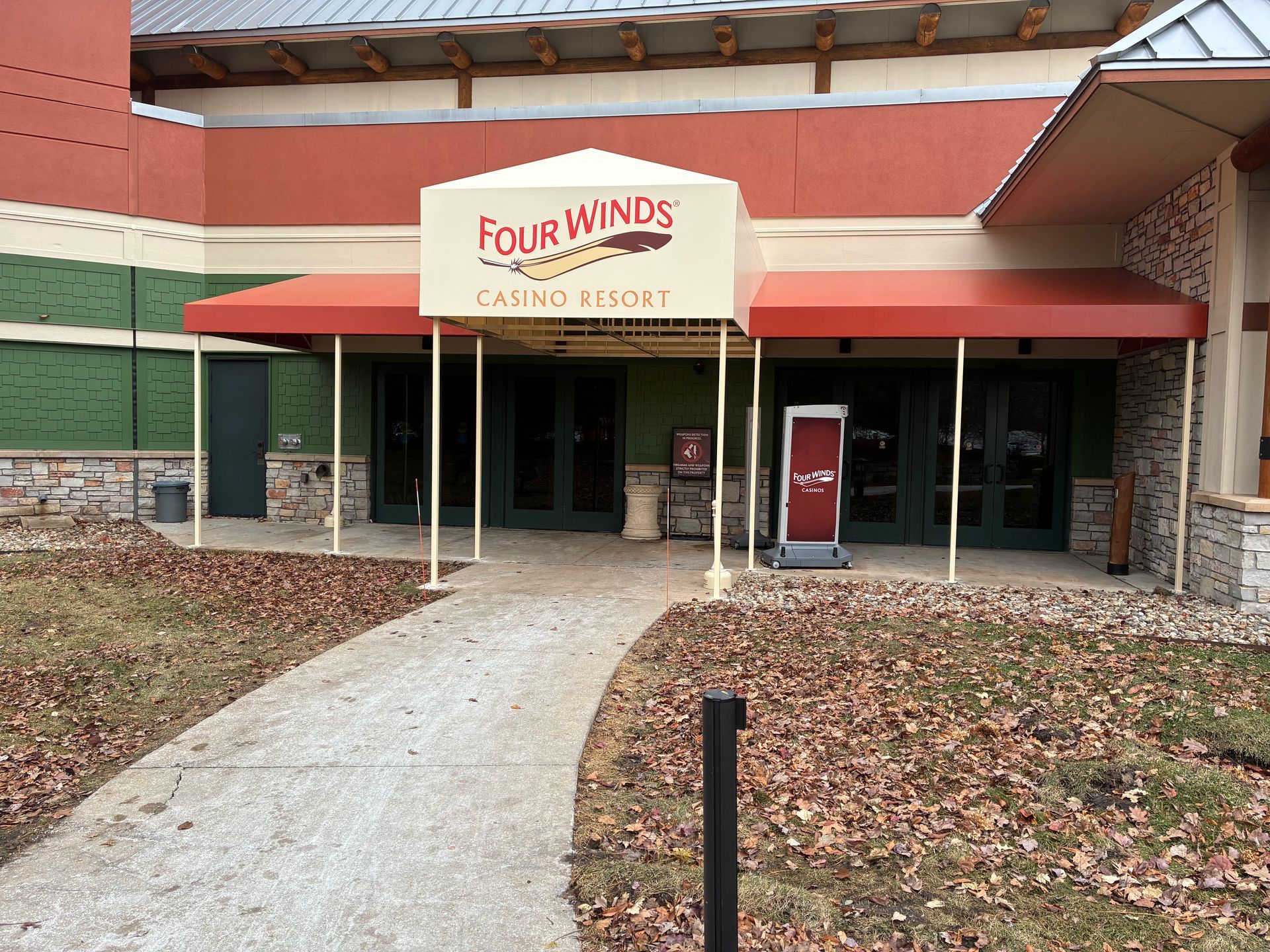 Entrance to Four Winds Studio Center with red awning and stone facade, surrounded by fallen leaves