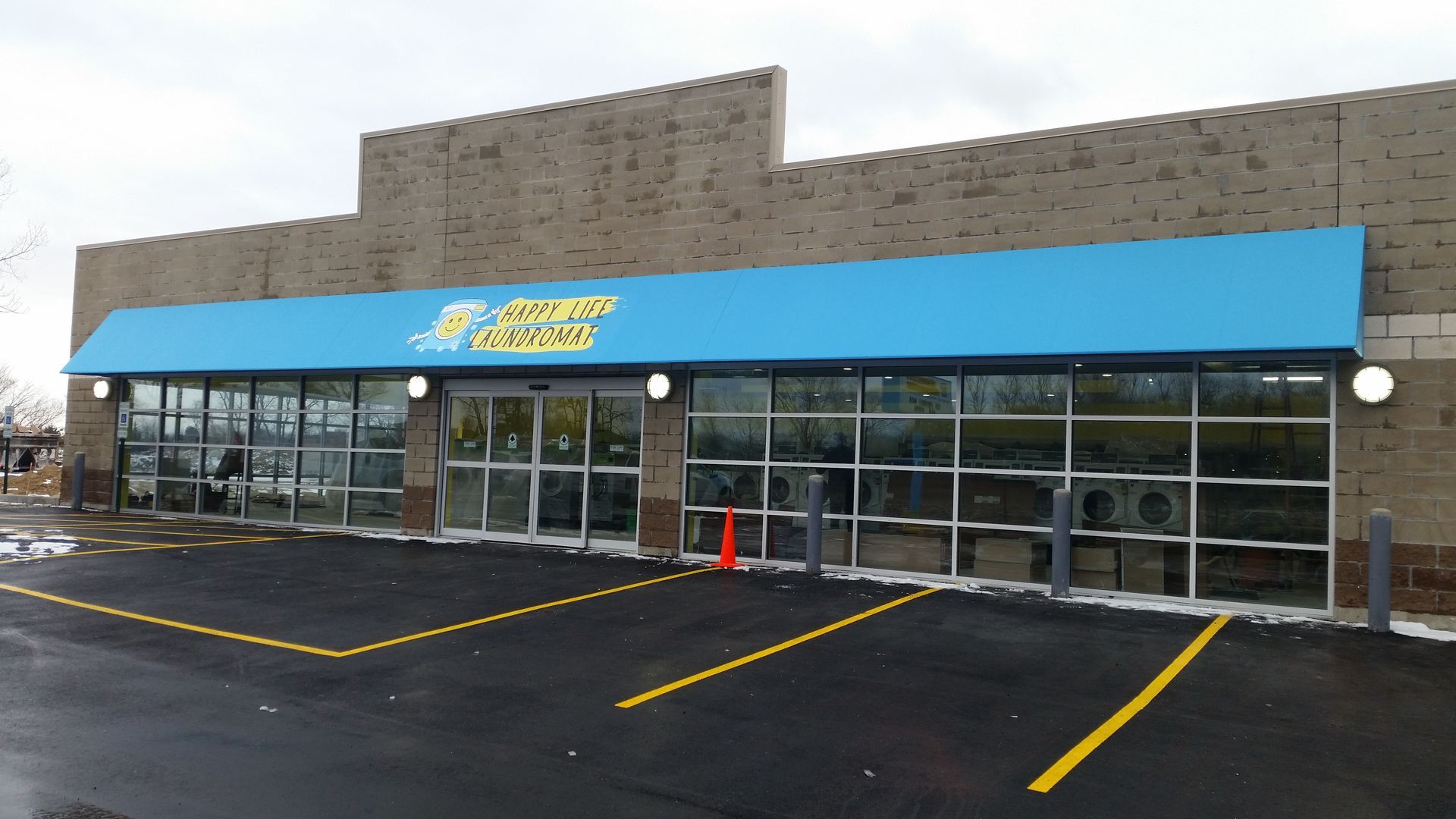 Strip mall storefront with blue awning, glass windows, and empty parking spaces on a wet day