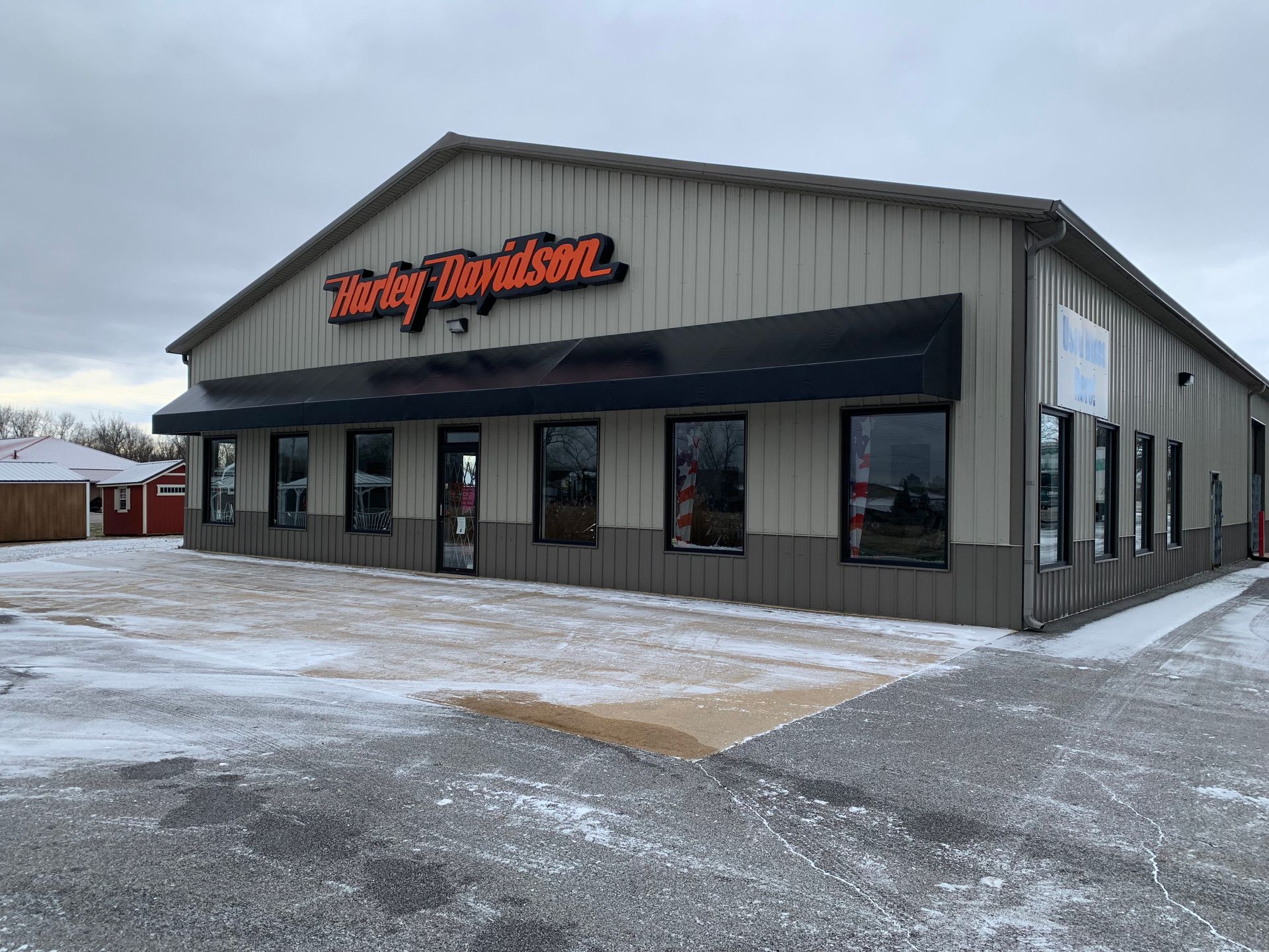 Harley-Davidson motorcycle dealership exterior with gray siding, black awning, and snowy parking lot