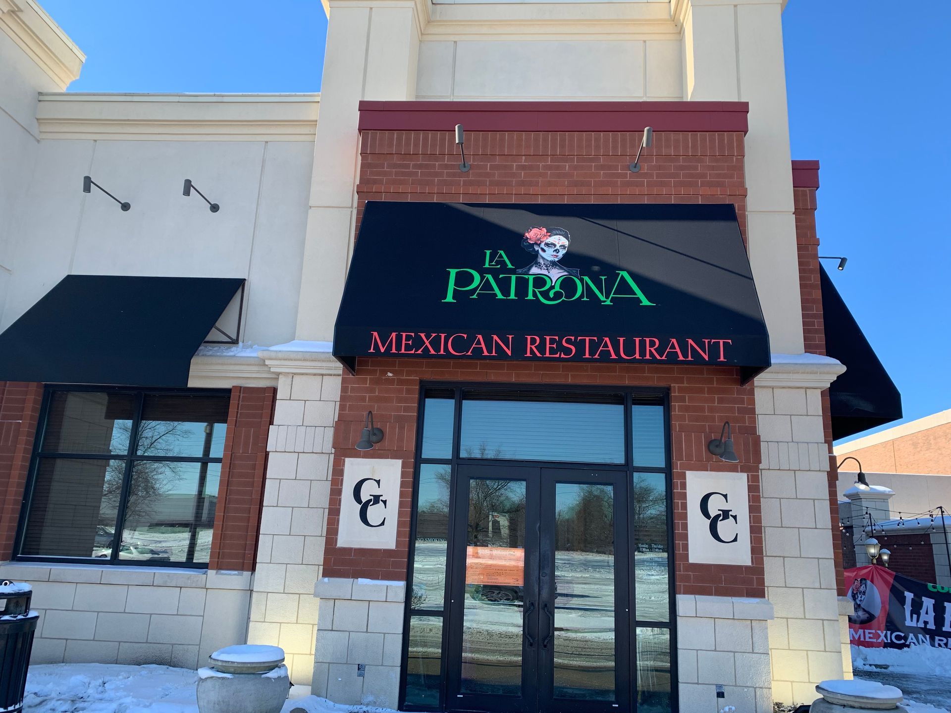 Restaurant entrance with black awning reading “Patrona Mexican Restaurant” on a beige building