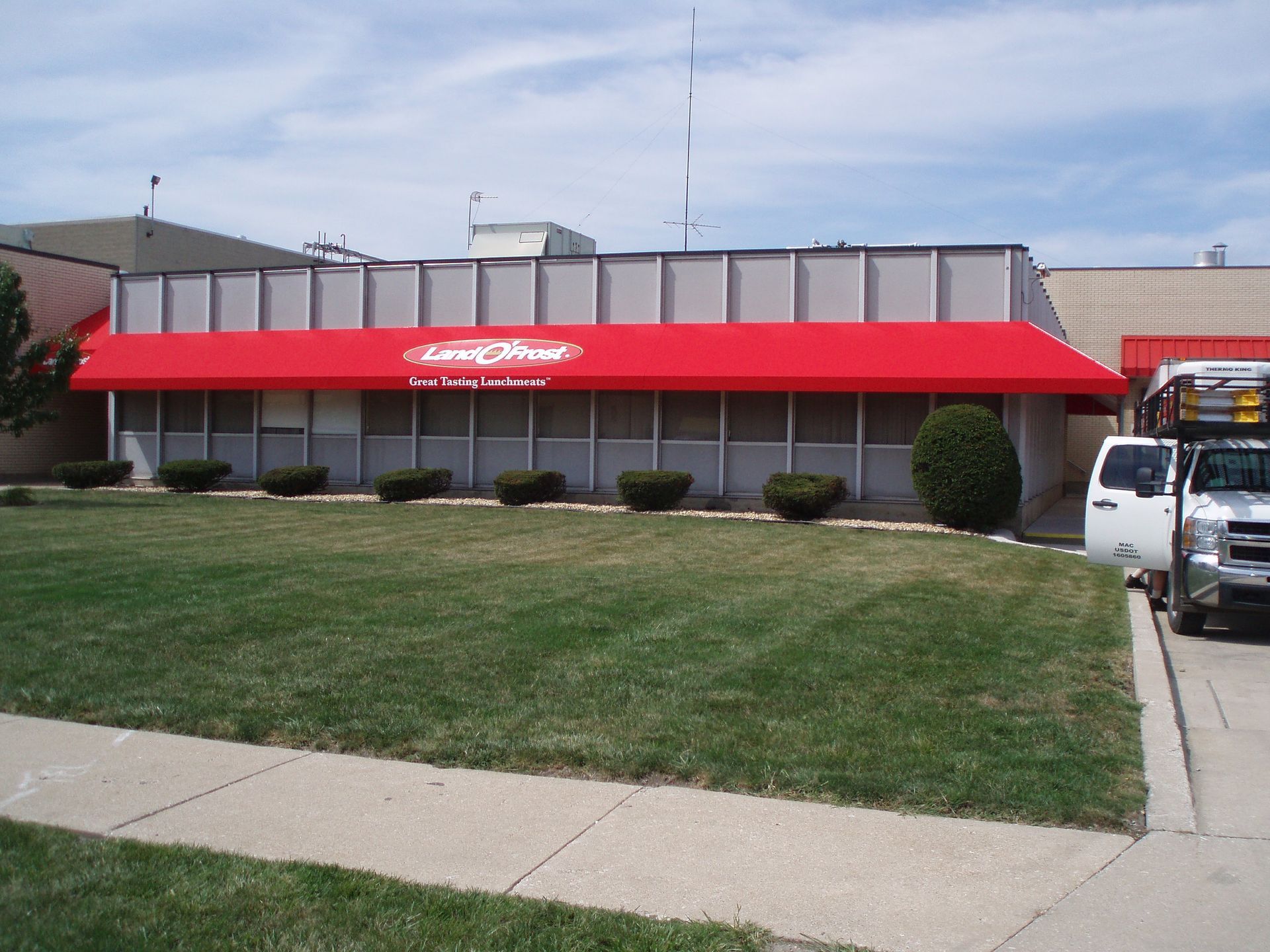 Storefront with red awning, grassy lawn, and parked vehicles in front