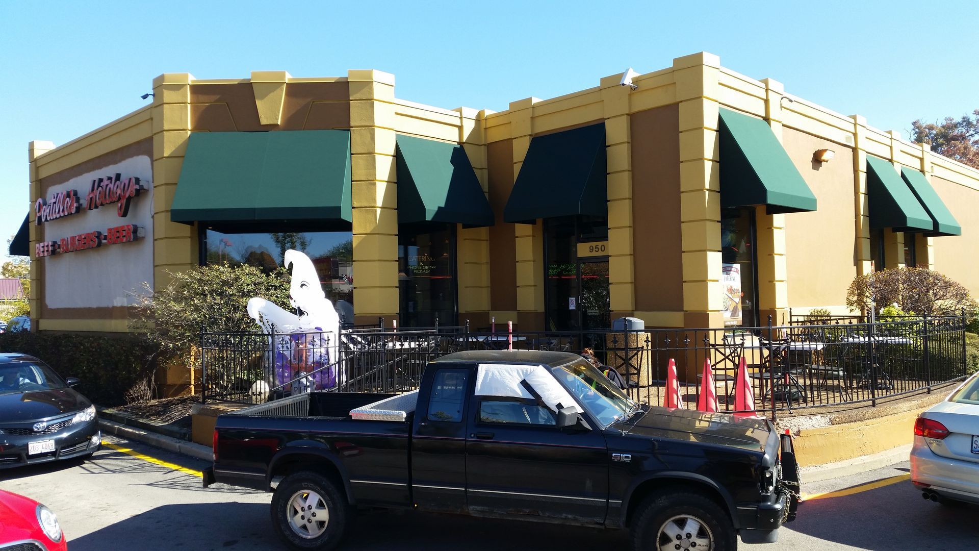 Restaurant exterior with green awnings, beige walls, and parked cars in front