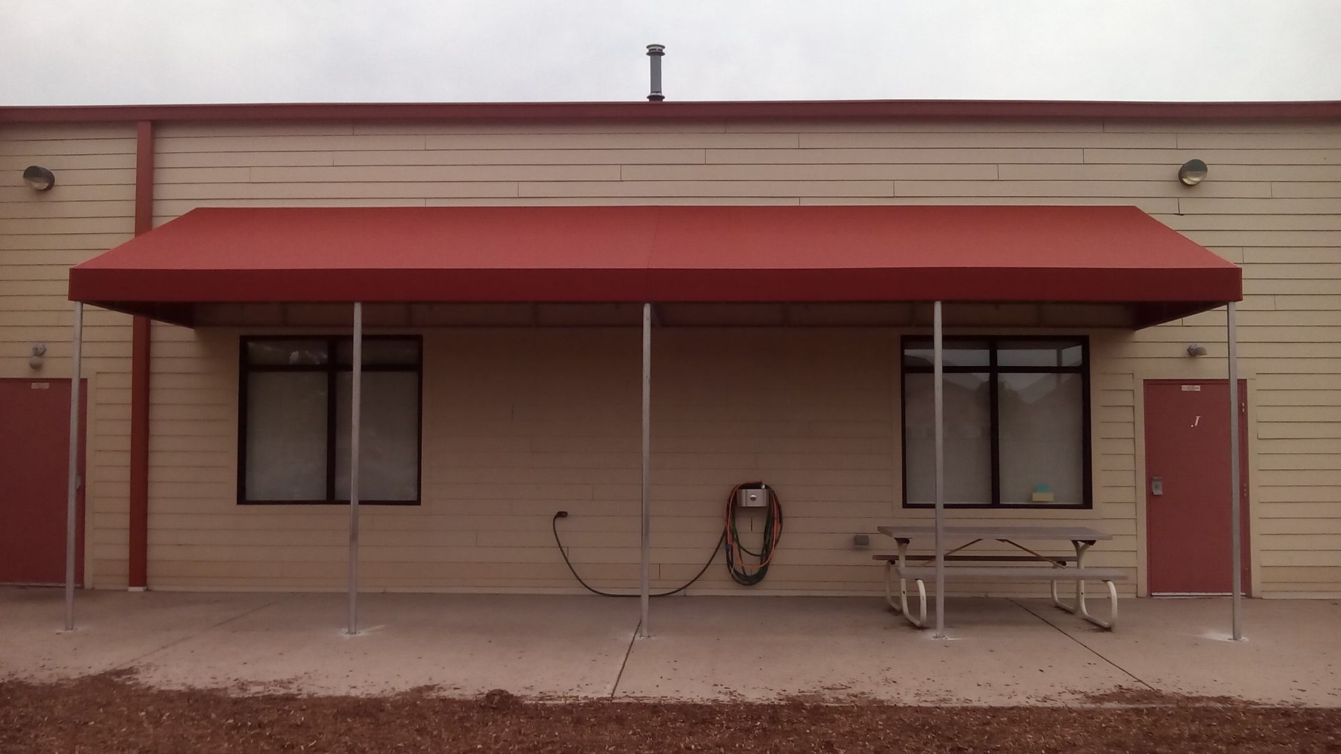 Brick building facade with a red awning, two windows, a door, and a bench on the walkway