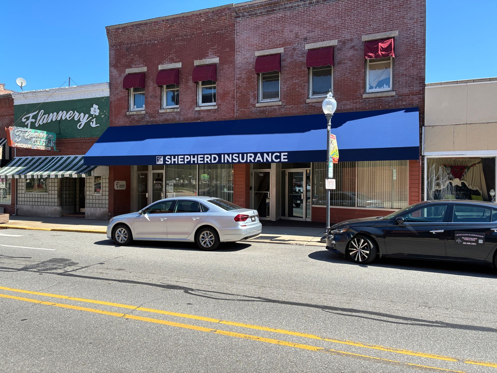 Brick storefronts on a sunny street, including 35th & Eberd Insurance, with parked cars in front