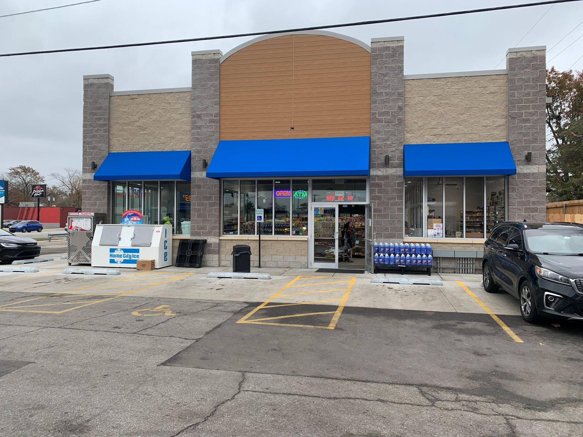 Storefront with blue awnings, glass doors, and parking spaces in front on an overcast day