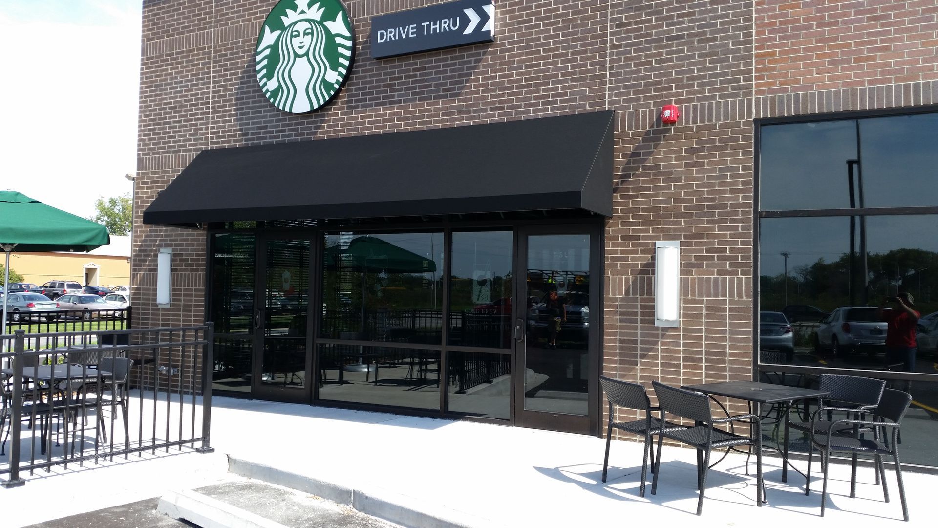 Starbucks storefront with black awning, glass windows, and outdoor seating on a sunny day