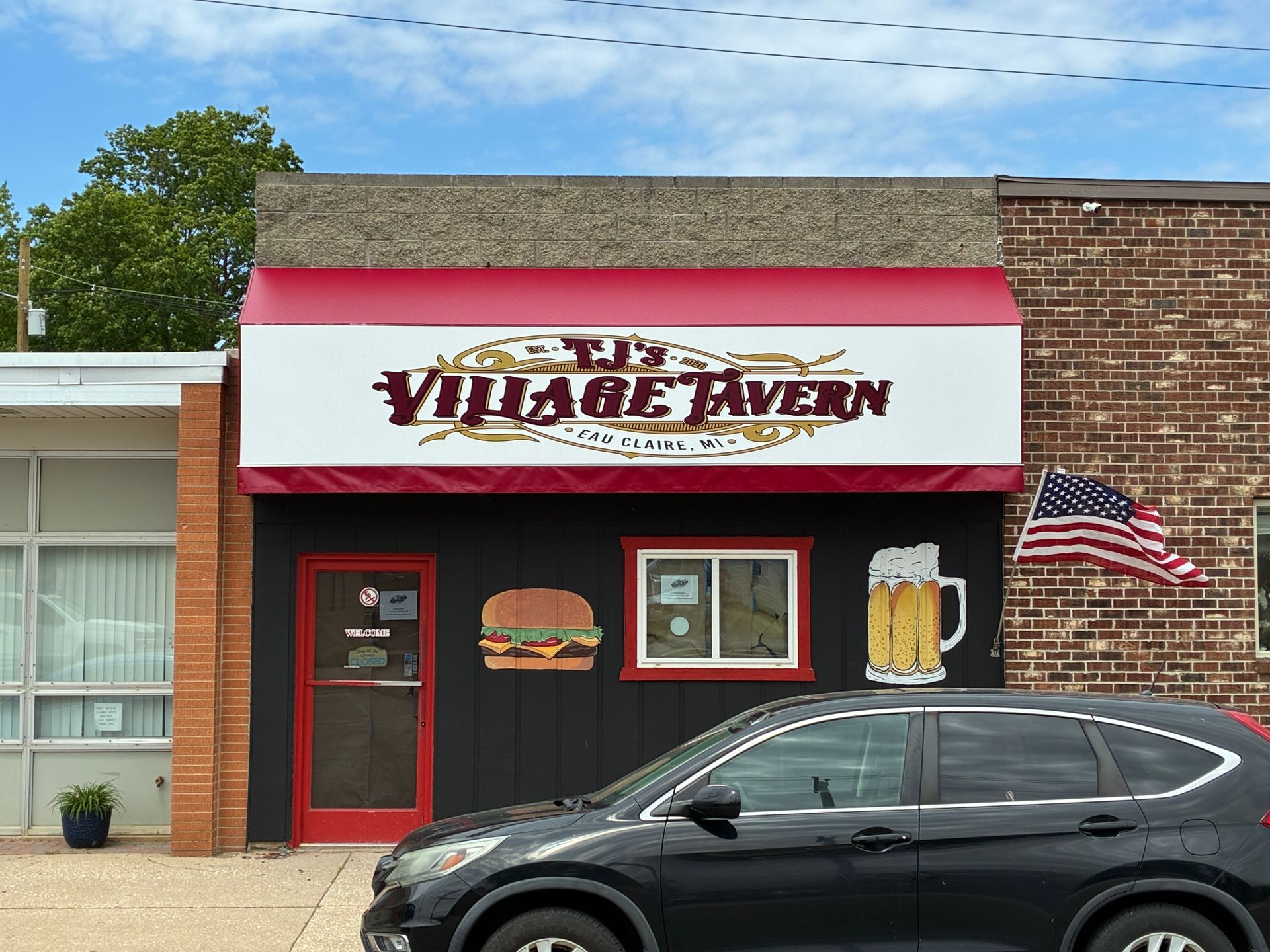Village Haven storefront with red trim, a black car parked in front, and an American flag on the brick wall