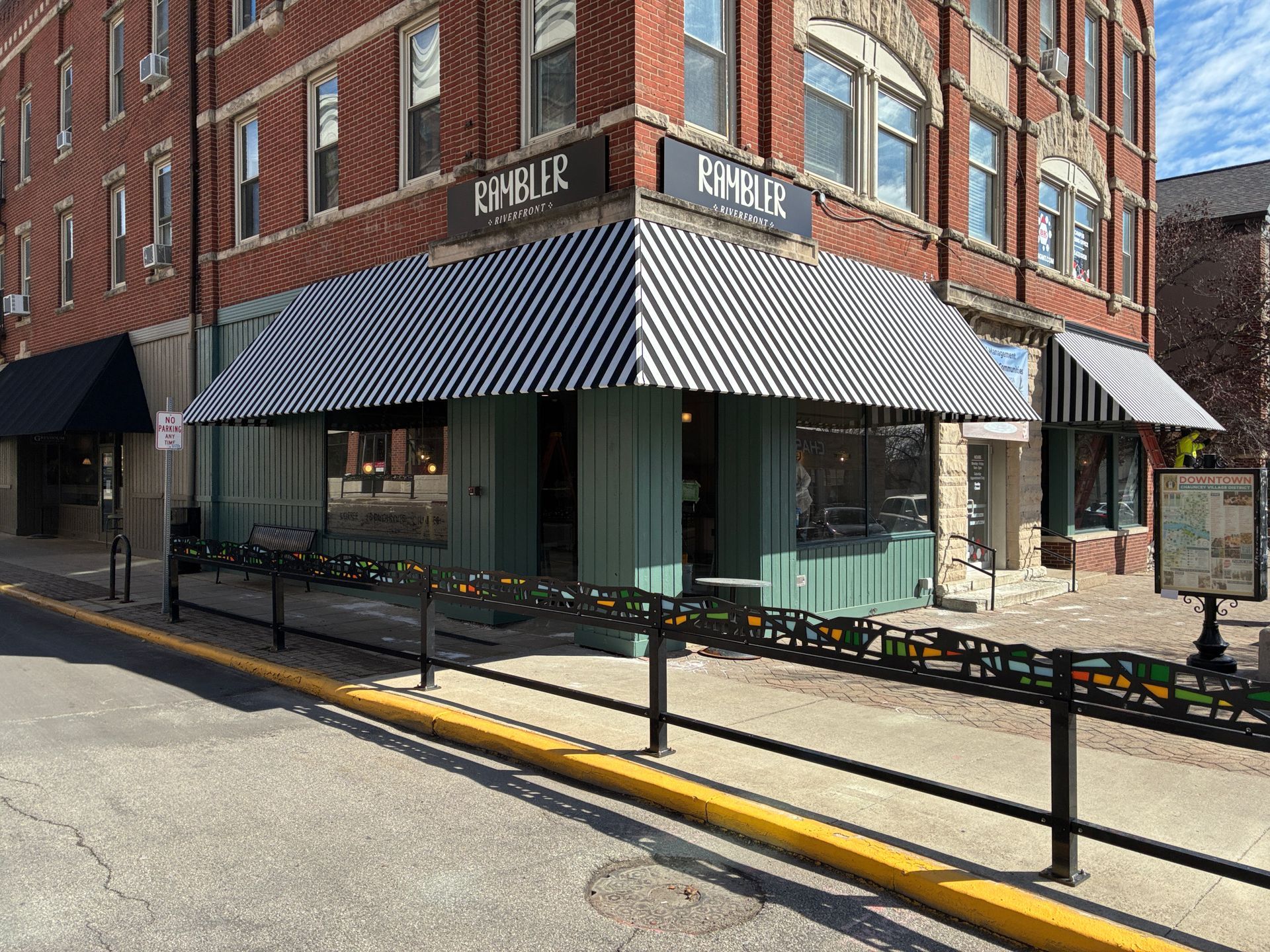 Corner café in a brick building with black-and-white striped awnings and outdoor seating on a sunny street