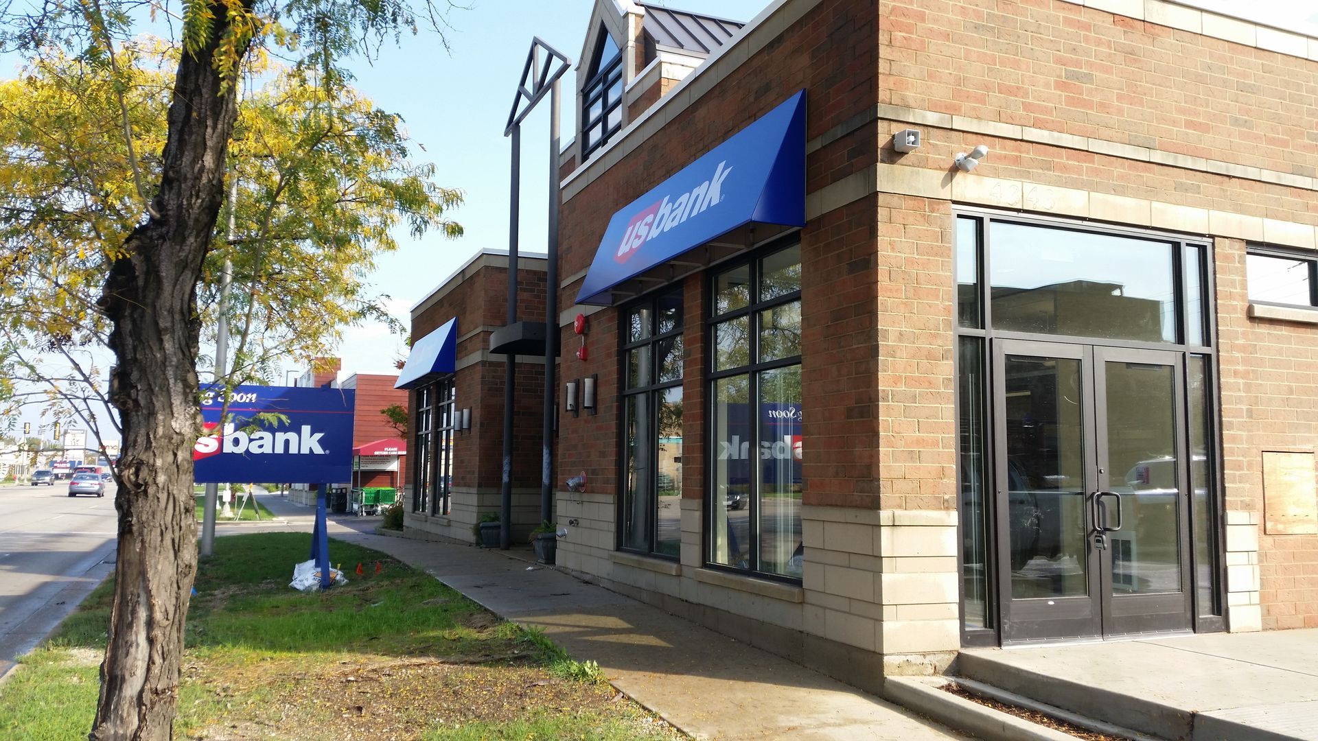 Bank branch storefront with blue awnings and glass doors on a sunny street corner