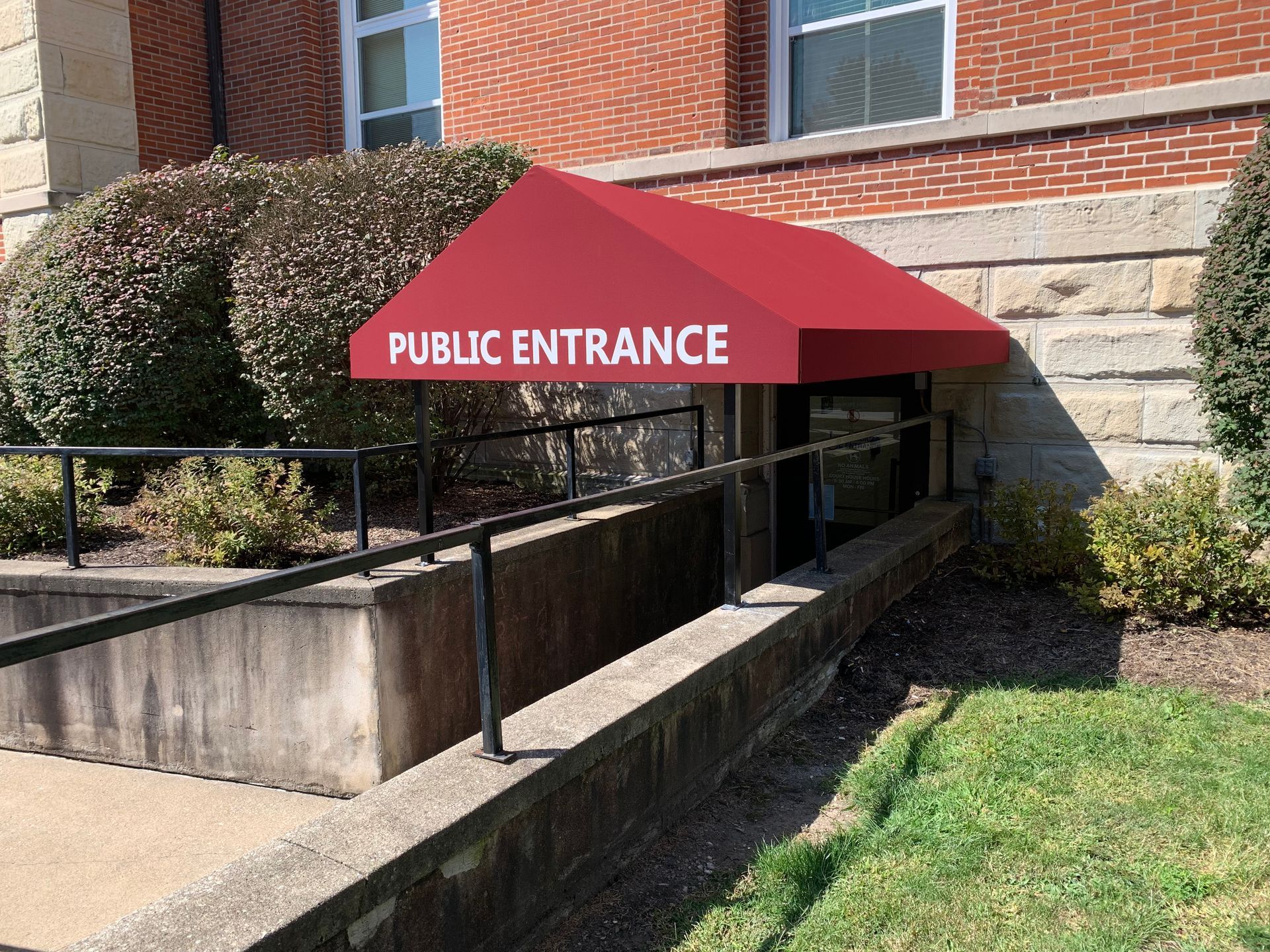 Red awning over accessible public entrance ramp beside a brick building