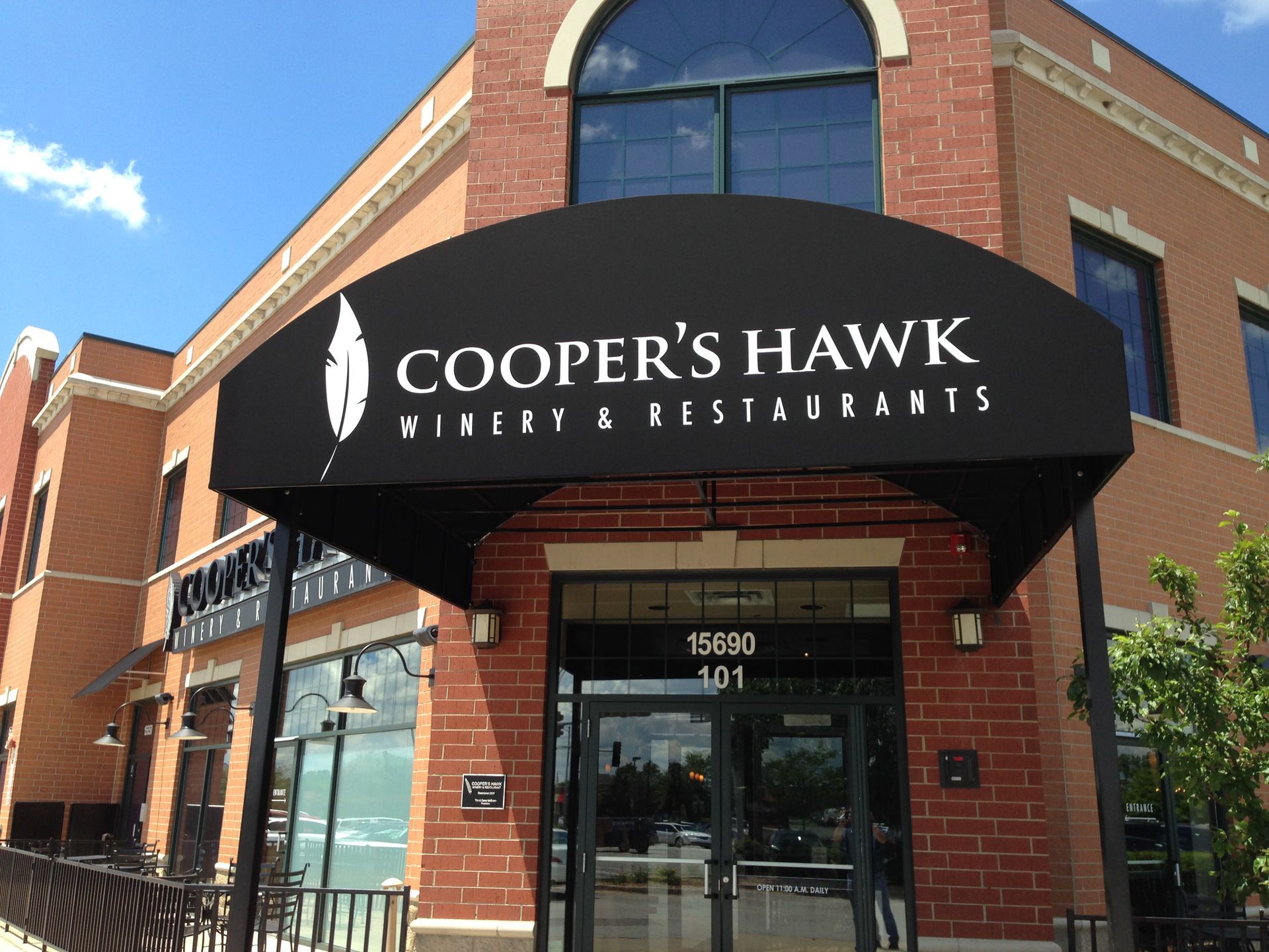 Cooper’s Hawk Winery & Restaurants storefront with black awning and glass entrance on a brick building