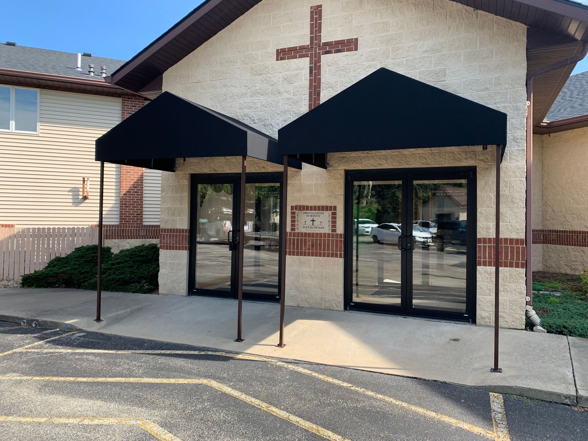 Church entrance with twin black awnings and glass double doors, brick cross above