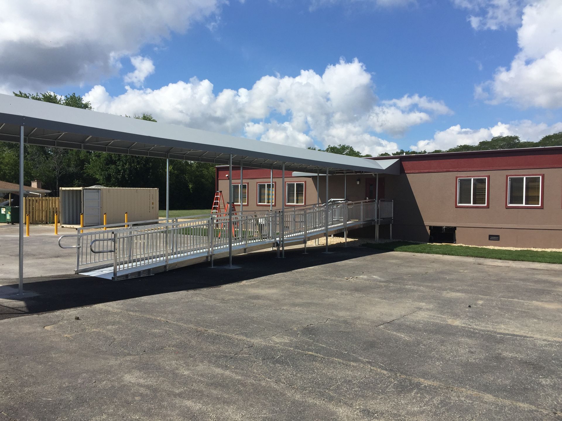 Accessible school ramp with railings beside a red building under a partly cloudy sky