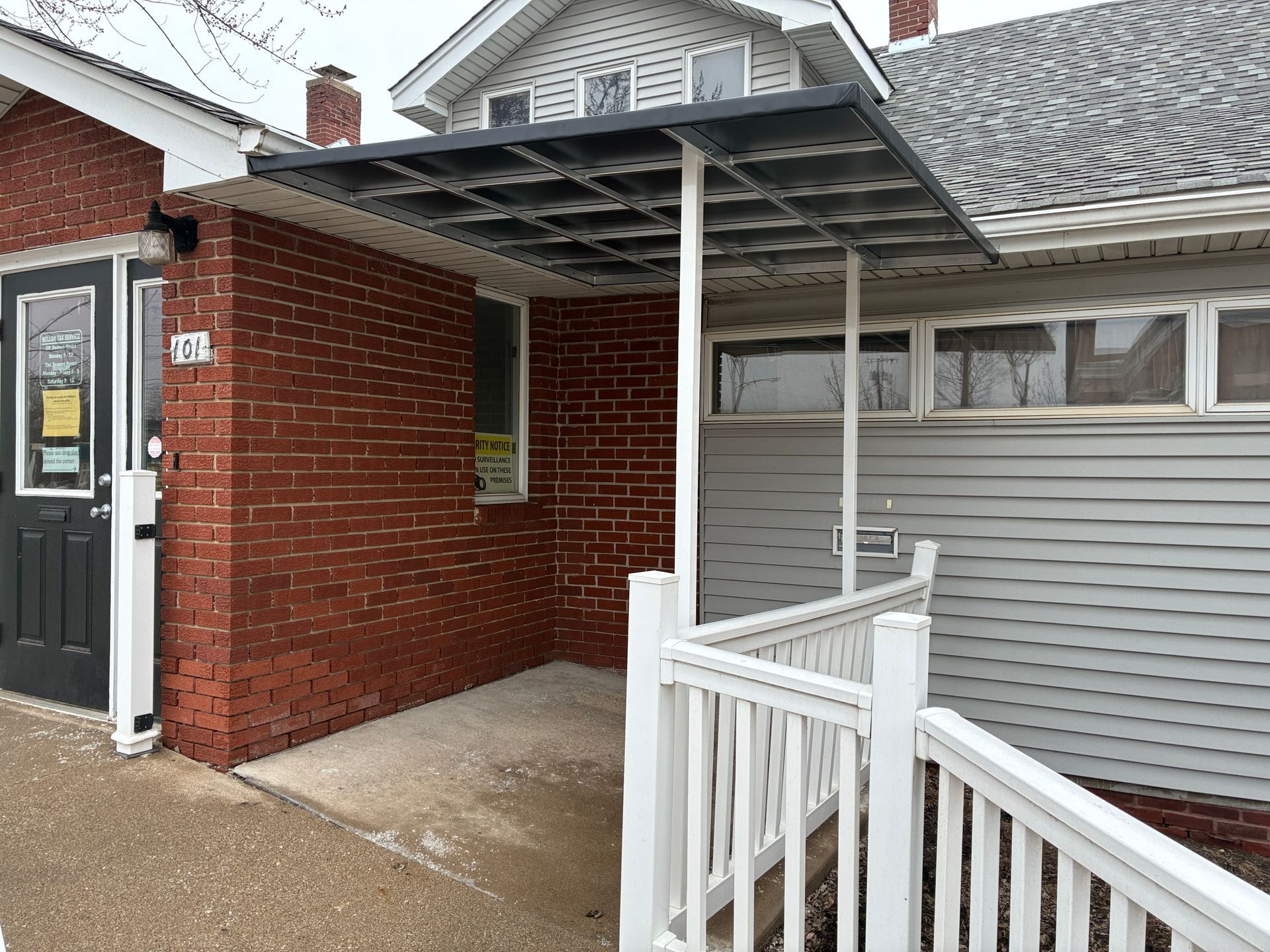 Covered entrance with white railing beside a red brick building and gray siding