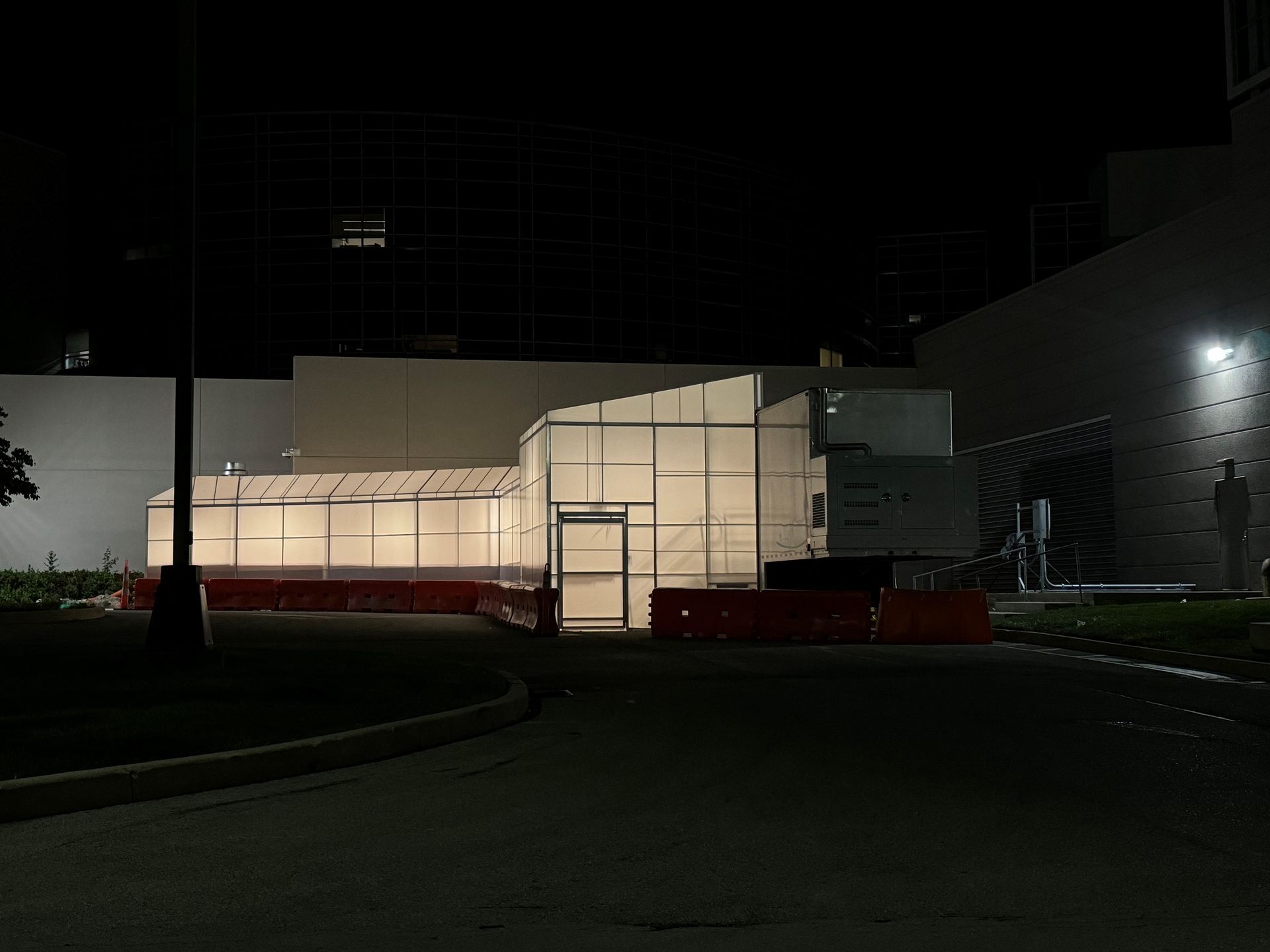 Night view of a white building with bright interior lights and red barriers along the front driveway