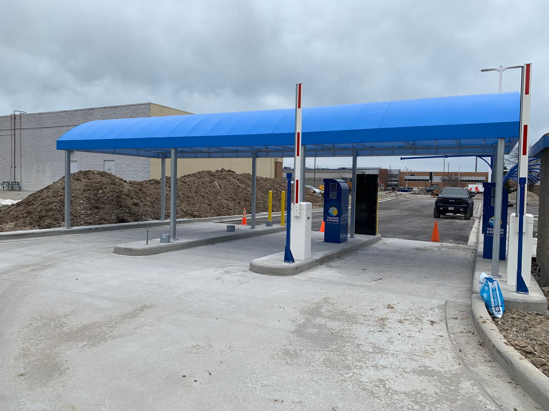 Blue-roofed car wash canopy with bays, a wash machine, and a parked car in a dusty lot