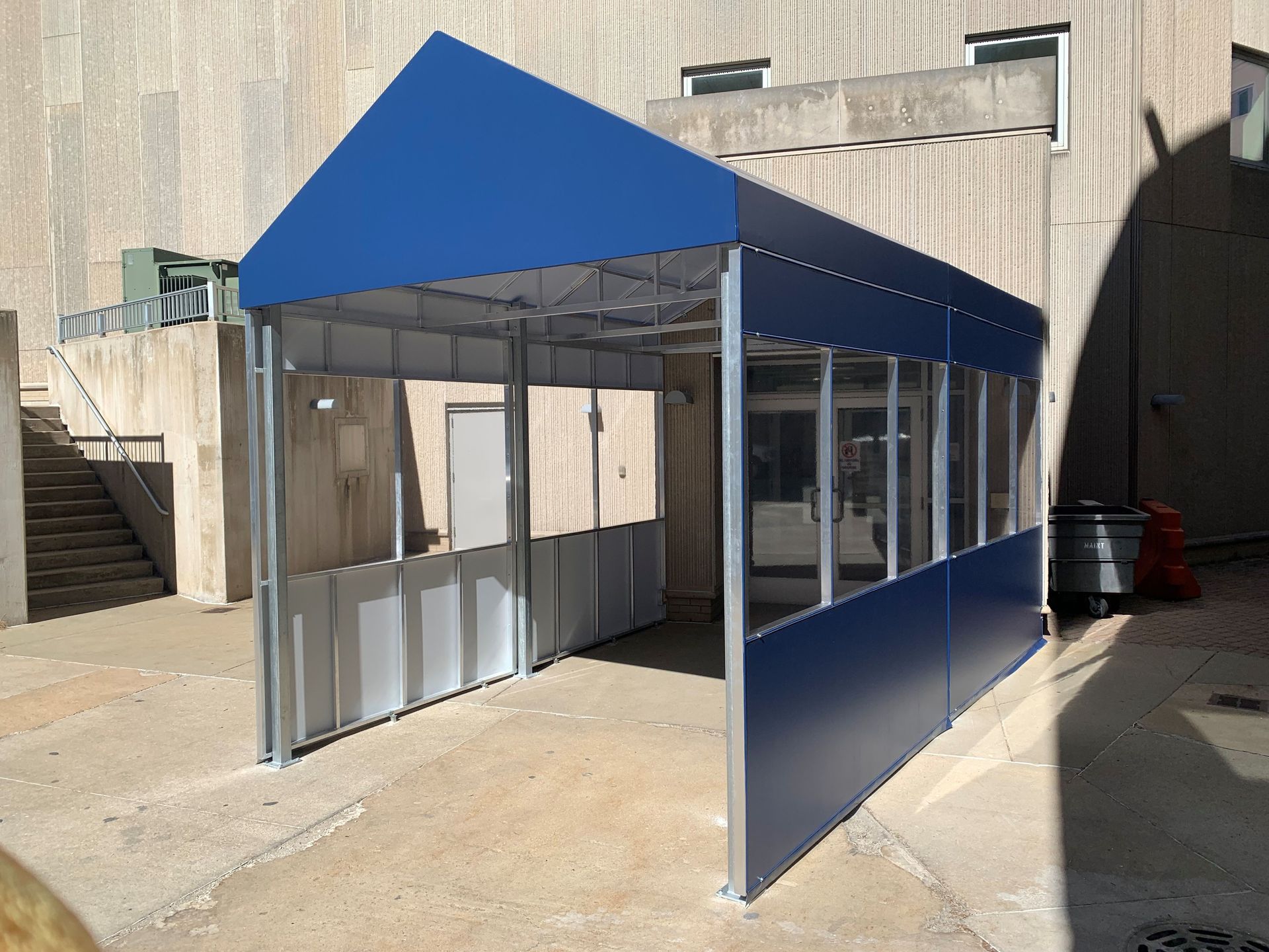 Blue tent-like shelter in an outdoor industrial area, with clear side panels and a metal frame.