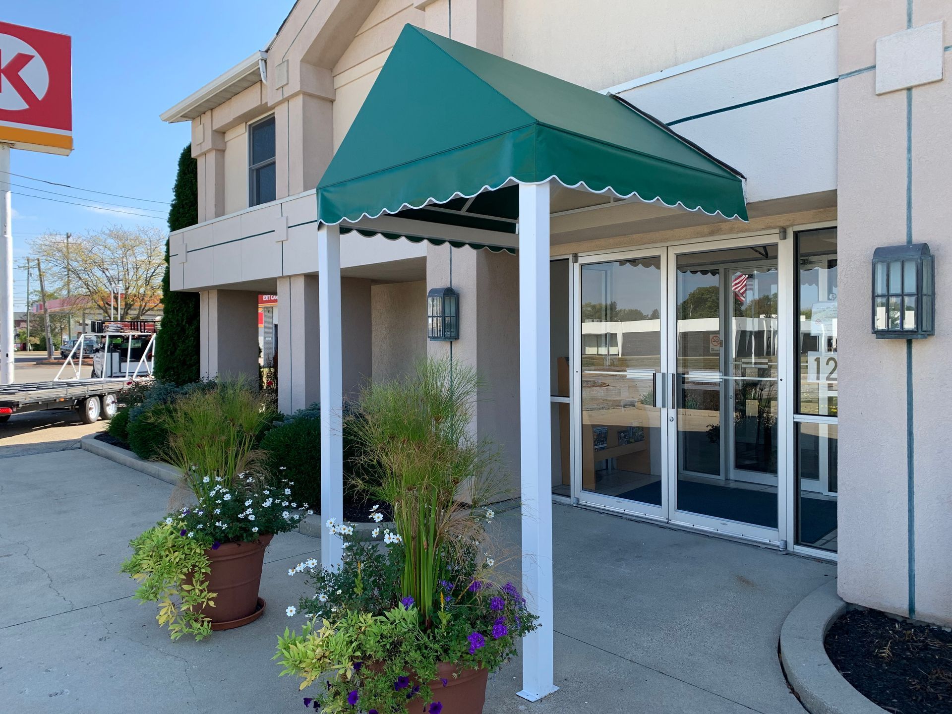 Storefront entrance with green awning, potted plants, and glass doors on a sunny sidewalk.