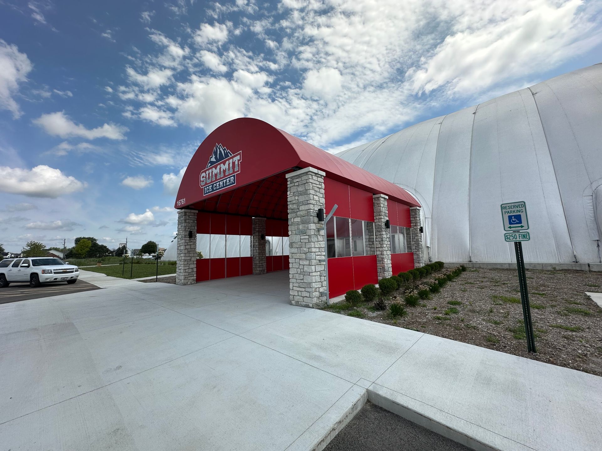 Small red-roofed building with stone columns beside a large white dome under a cloudy sky.
