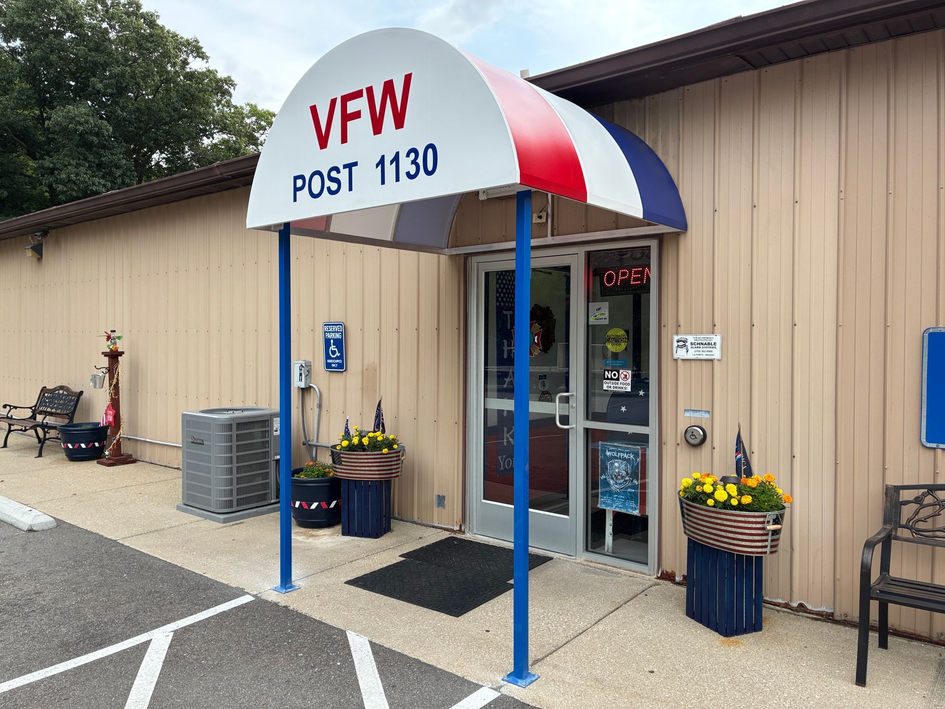 VFW Post 1130 entrance with blue-and-red awning, glass door, and potted flowers by beige siding