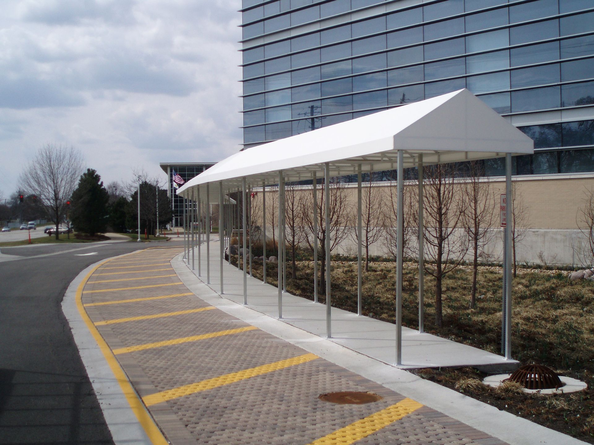 Covered sidewalk beside a modern building with yellow crosswalk stripes and curbside parking area