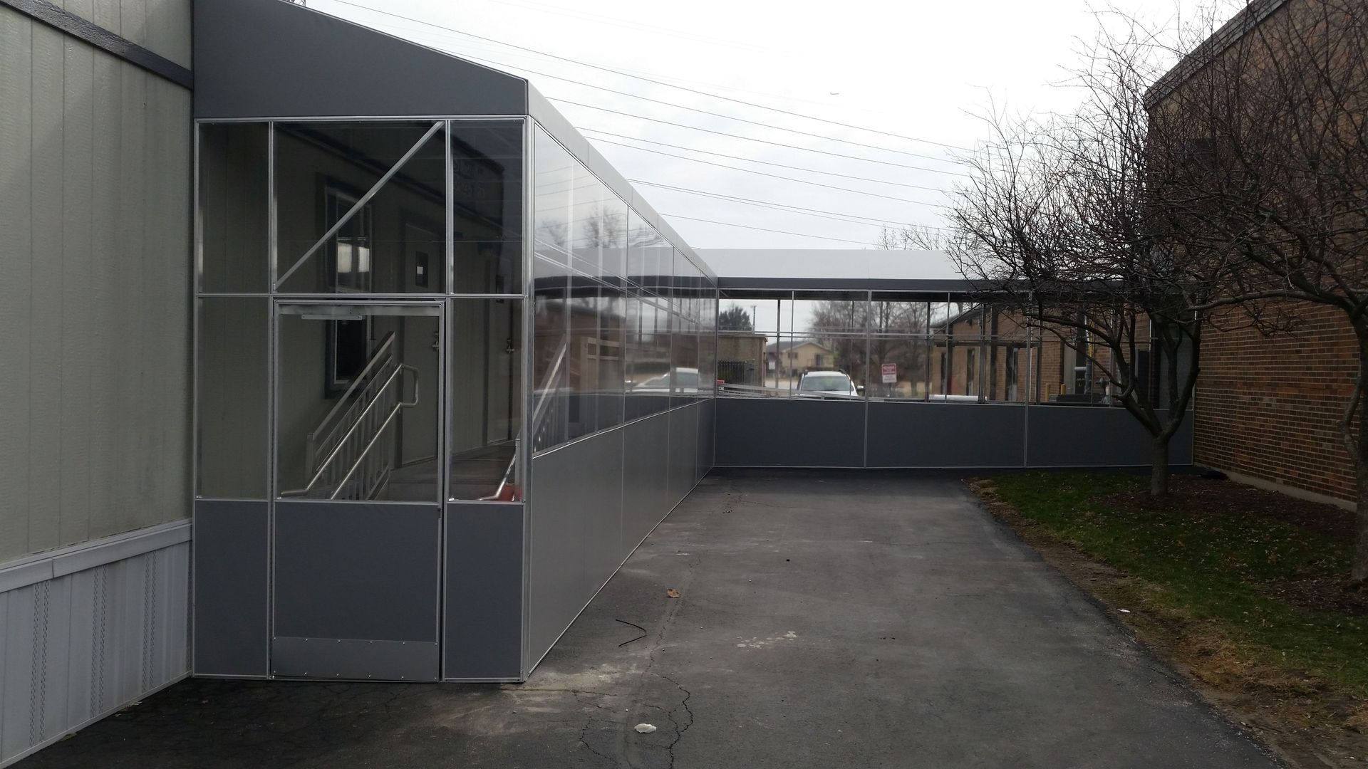 Exterior walkway beside a gray building with metal stairs, leading to a fenced area under an overcast sky