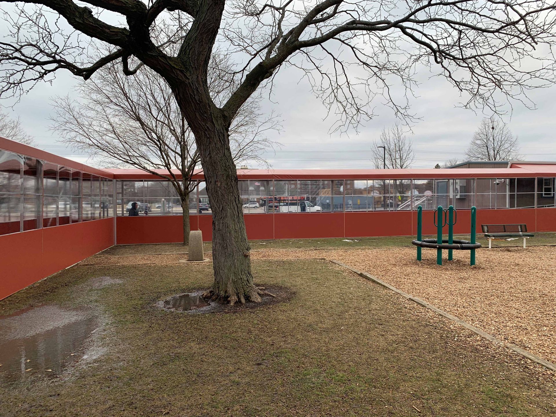 Empty school courtyard with a leafless tree, red buildings, and a playground on a gray day
