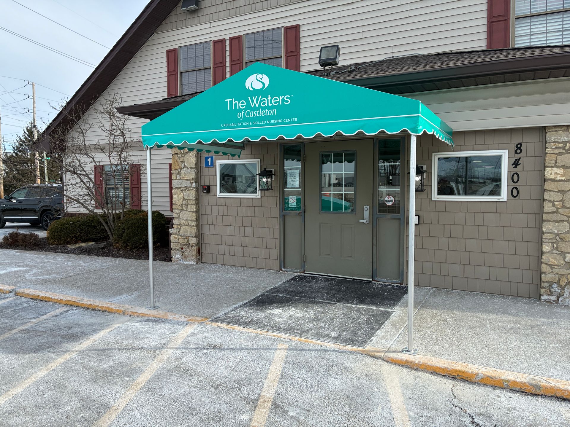 Entrance with turquoise awning reading “The Grill,” over double doors at a building facade.