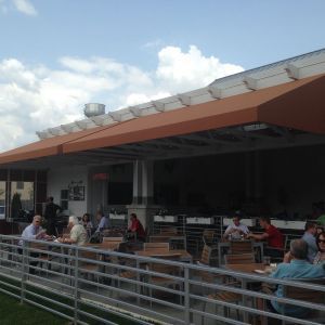 Outdoor cafe patio with seated diners under a long orange roof and metal railing in front