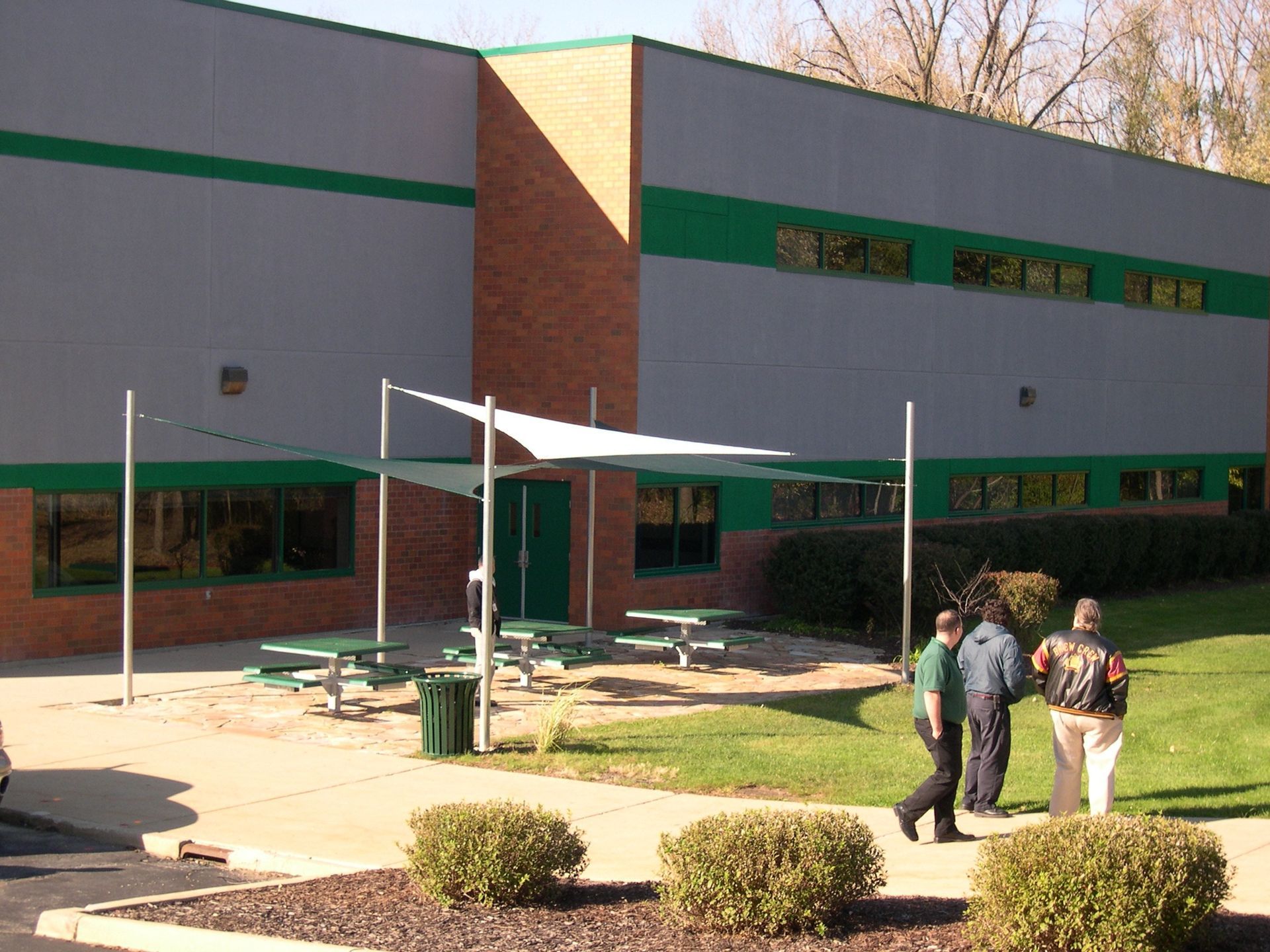 People standing outside a brick building with green trim near a courtyard.