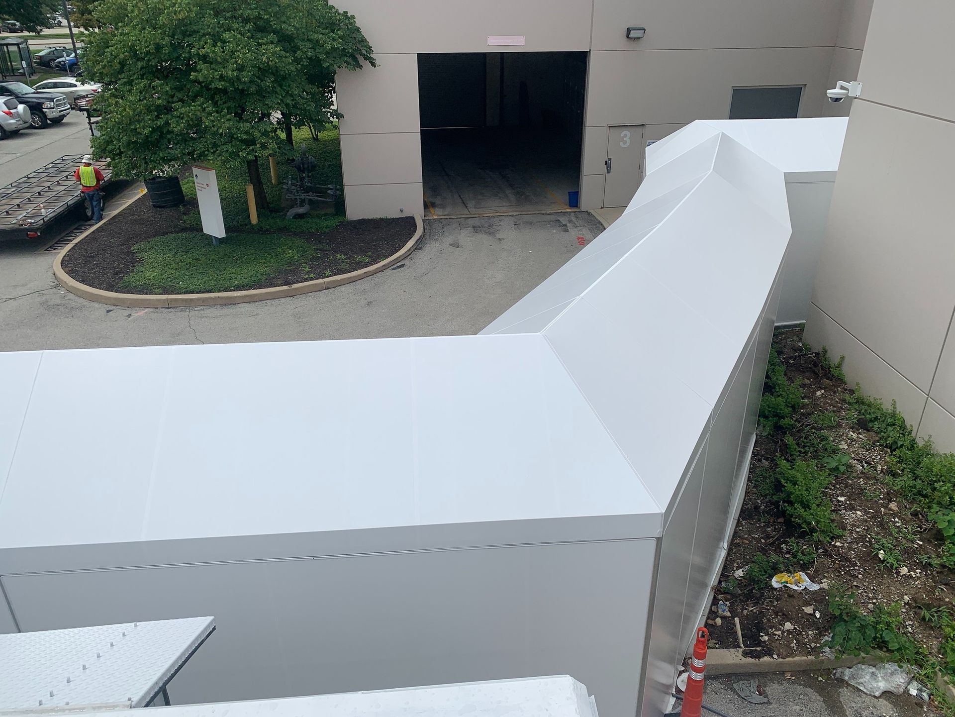 White covered outdoor ramp with a sharp turn beside a building entrance and landscaped area
