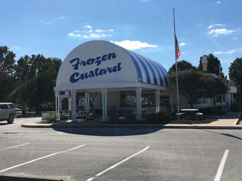 Frozen Custard stand with a striped dome roof and American flag in a sunny parking lot
