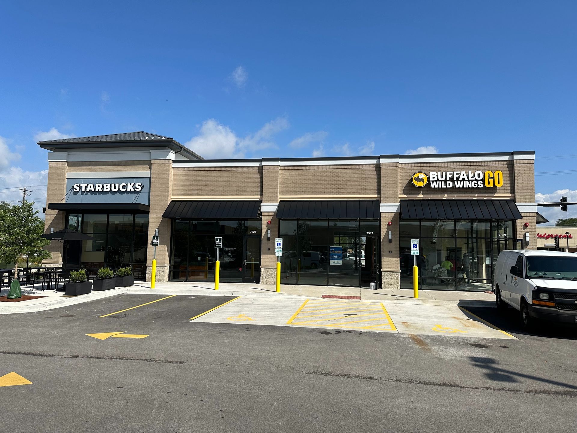 Strip mall storefronts with Starbucks and Dollar Tree under a blue sky, with parked cars in front.